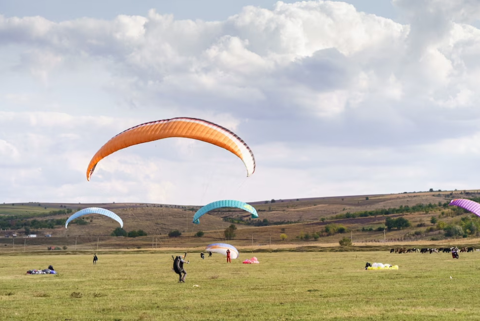 paragliders on a green landscape under a blue sky with clouds