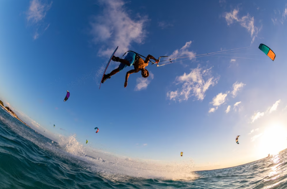 person surfing and flying a parachute at the same time, other skydivers on the ocean waves