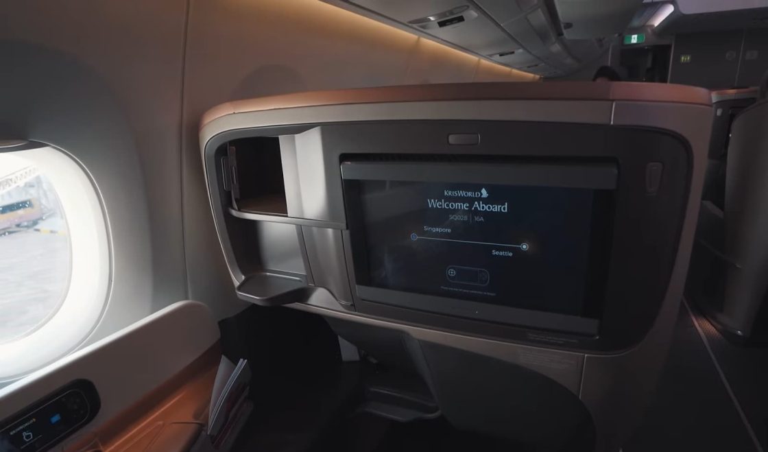 a small TV in front of the seat in the airplane and a small window in the corner